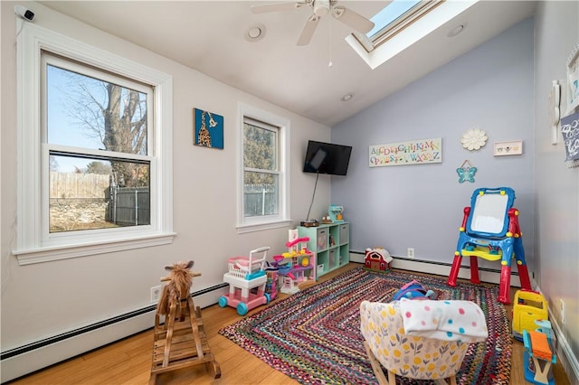 rec room featuring a ceiling fan, vaulted ceiling with skylight, baseboard heating, and wood finished floors