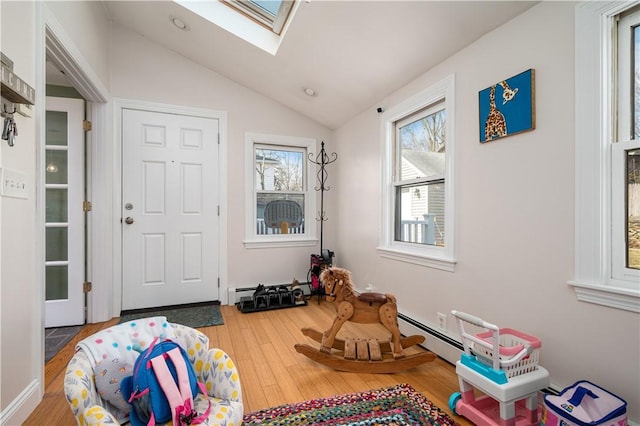 recreation room with a baseboard radiator, vaulted ceiling with skylight, and wood finished floors