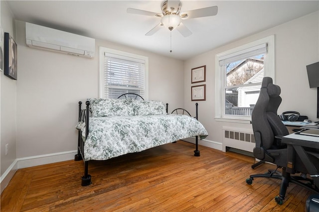 bedroom with radiator, light wood-type flooring, baseboards, and a wall mounted AC