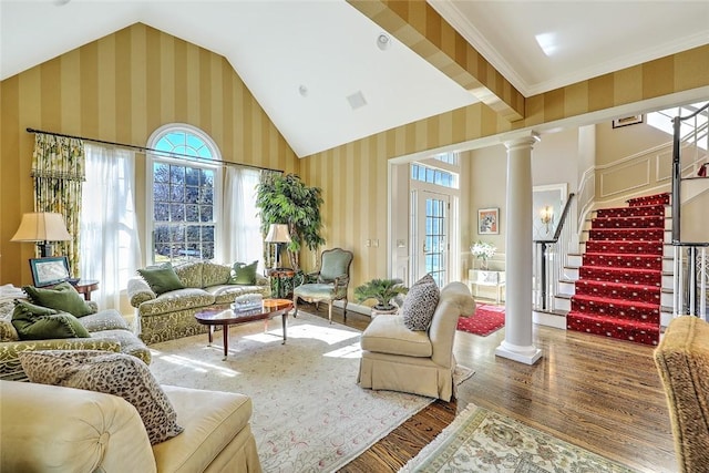 living room with high vaulted ceiling, wood finished floors, stairs, decorative columns, and wallpapered walls