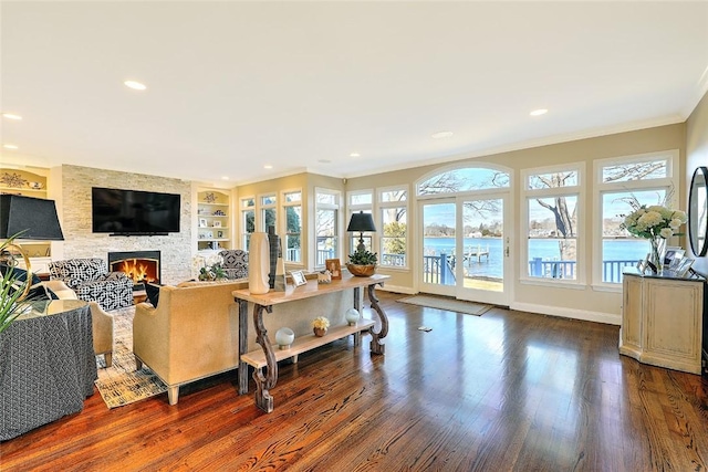 living area featuring built in shelves, dark wood-style flooring, ornamental molding, a large fireplace, and baseboards