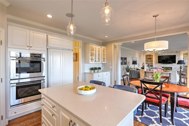 kitchen featuring stainless steel double oven, crown molding, hanging light fixtures, and ornate columns