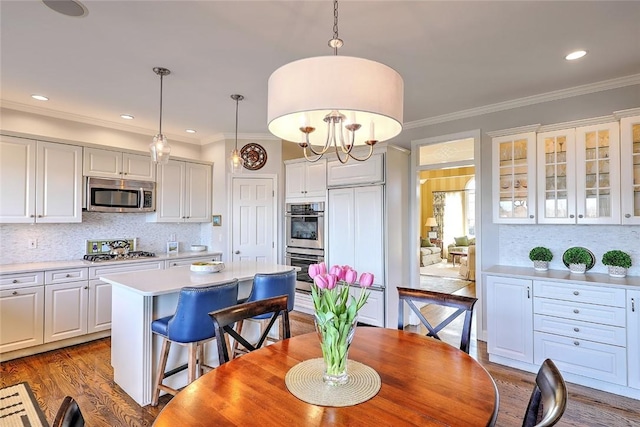 kitchen featuring a kitchen island, appliances with stainless steel finishes, ornamental molding, wood finished floors, and light countertops