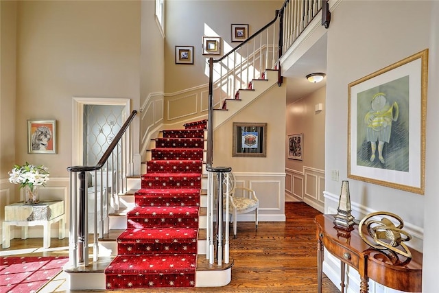 staircase featuring a high ceiling, wainscoting, wood finished floors, and a decorative wall