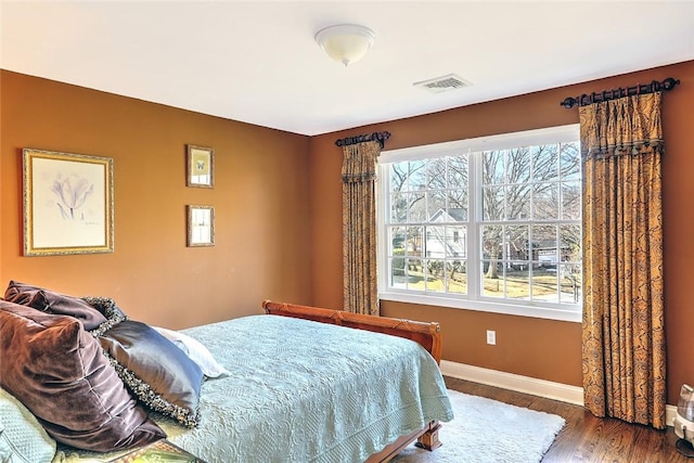 bedroom with wood finished floors, visible vents, and baseboards