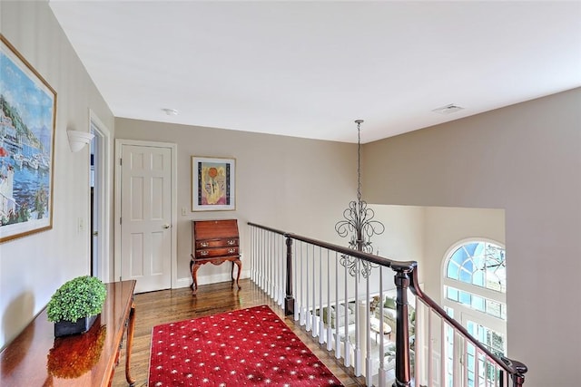 hall featuring baseboards, visible vents, wood finished floors, an upstairs landing, and a chandelier