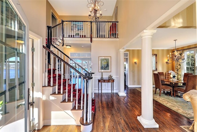 foyer featuring stairs, a notable chandelier, ornate columns, and wood finished floors