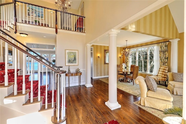 entryway with a notable chandelier, wood finished floors, a towering ceiling, and ornate columns