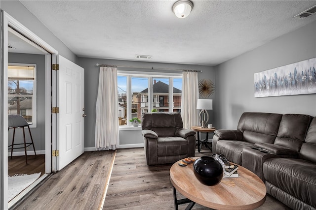 living area featuring a wealth of natural light, visible vents, and wood finished floors