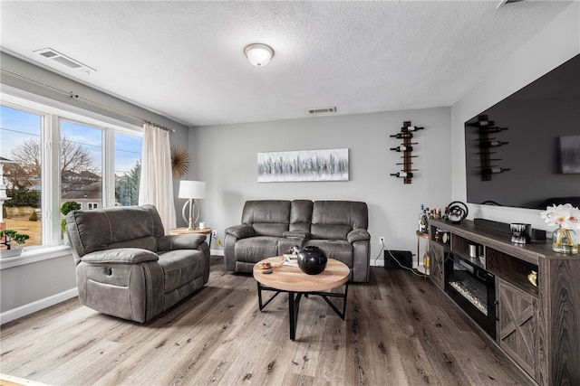 living room with baseboards, a textured ceiling, visible vents, and wood finished floors