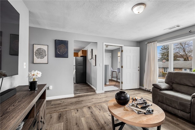 living area with a textured ceiling, light wood-style flooring, visible vents, and baseboards