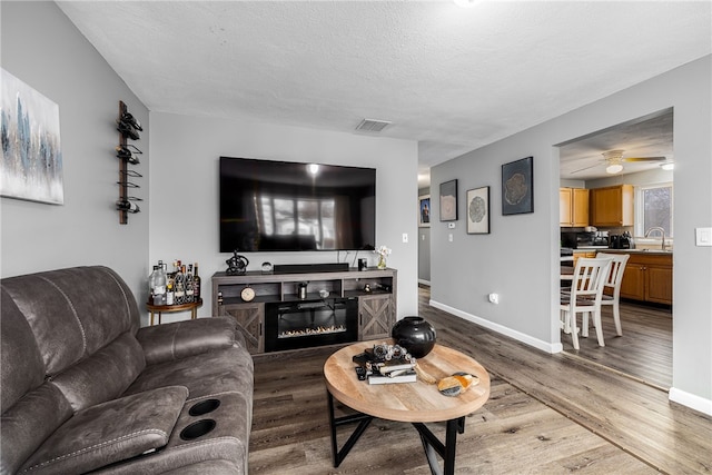 living room with a glass covered fireplace, a textured ceiling, baseboards, and wood finished floors