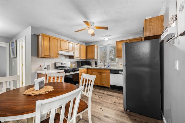 kitchen with under cabinet range hood, stainless steel appliances, light countertops, light wood-type flooring, and tasteful backsplash