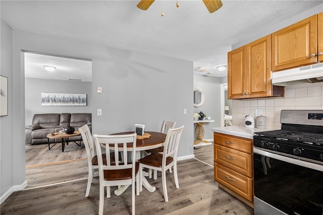 kitchen with tile countertops, under cabinet range hood, light wood finished floors, tasteful backsplash, and gas range