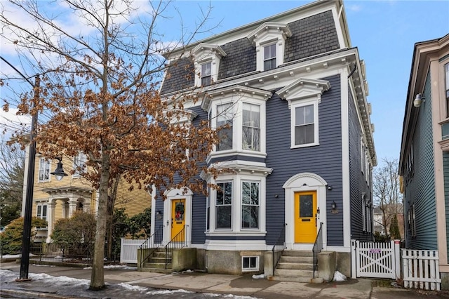 second empire-style home featuring entry steps, a gate, fence, and mansard roof