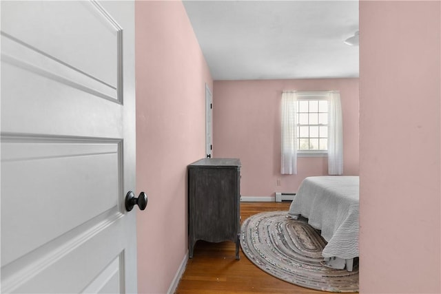 bedroom with baseboard heating, wood finished floors, and baseboards