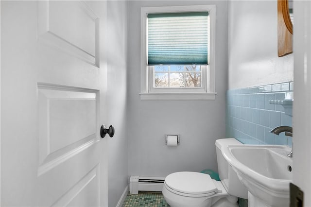 half bathroom with a sink, toilet, tile walls, and baseboard heating