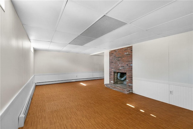 below grade area featuring a drop ceiling, wood finished floors, a baseboard radiator, and a brick fireplace