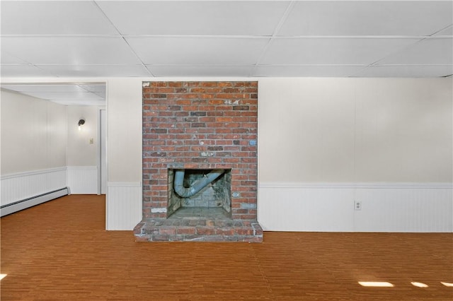 unfurnished living room with a brick fireplace, a drop ceiling, baseboard heating, and wood finished floors