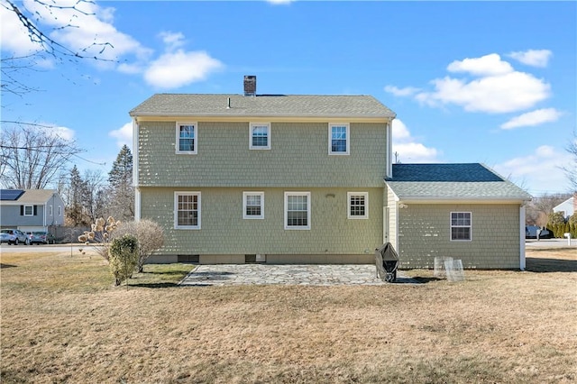 rear view of property featuring a chimney, a lawn, and roof with shingles