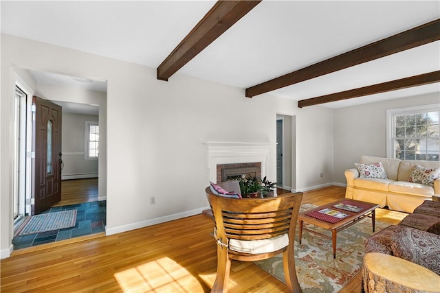 living room featuring a brick fireplace, beamed ceiling, baseboards, and wood finished floors