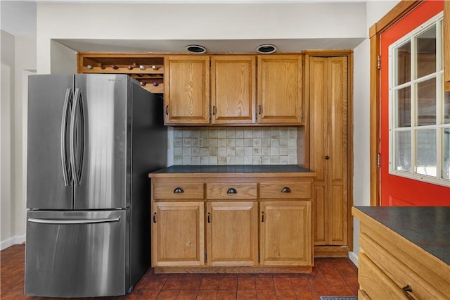 kitchen featuring dark countertops, brown cabinets, freestanding refrigerator, and decorative backsplash