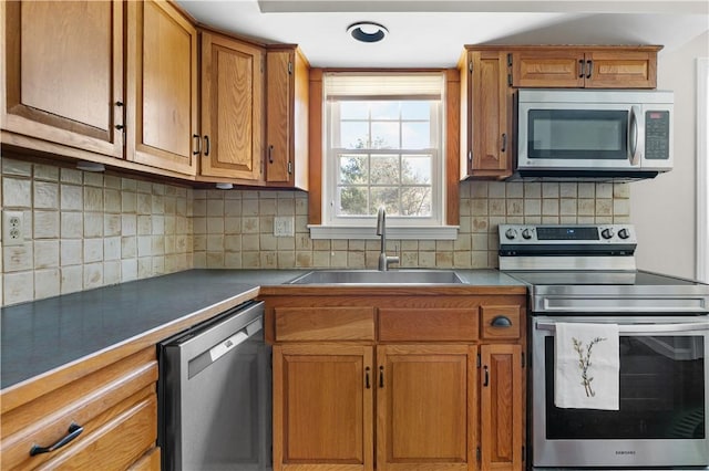 kitchen with tasteful backsplash, dark countertops, appliances with stainless steel finishes, brown cabinets, and a sink