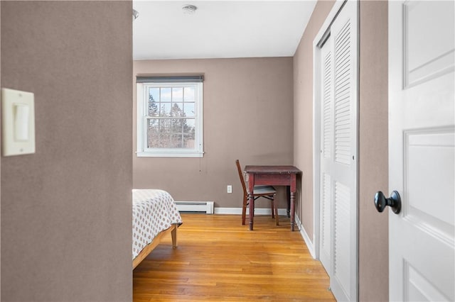 bedroom with light wood finished floors, a closet, a baseboard radiator, and baseboards