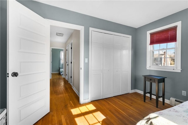 bedroom featuring wood finished floors, visible vents, baseboards, a closet, and baseboard heating