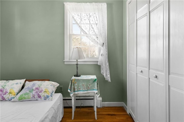 bedroom with a baseboard heating unit, baseboards, and wood finished floors