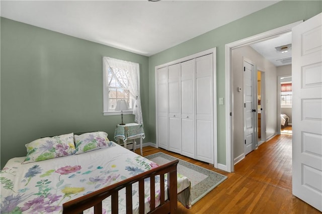 bedroom featuring a closet, multiple windows, baseboards, and wood finished floors