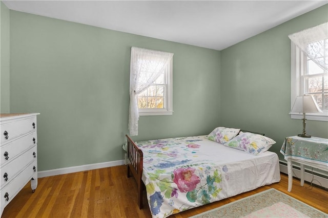 bedroom with a baseboard radiator, baseboards, and wood finished floors