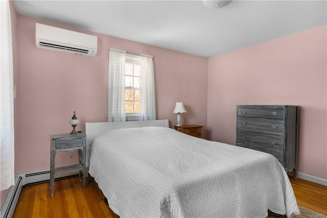 bedroom with a baseboard heating unit, an AC wall unit, baseboards, and wood finished floors