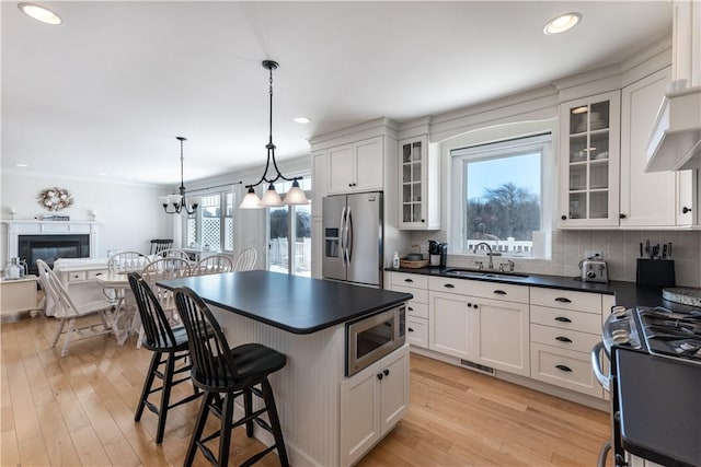 kitchen featuring stainless steel appliances, dark countertops, a sink, light wood-type flooring, and a kitchen breakfast bar