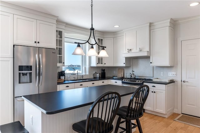 kitchen featuring a breakfast bar area, dark countertops, glass insert cabinets, a sink, and stainless steel fridge with ice dispenser