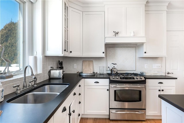 kitchen with a sink, dark countertops, stainless steel range with gas cooktop, and white cabinetry