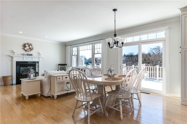 dining space with a glass covered fireplace, crown molding, and light wood finished floors