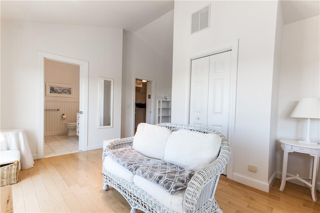 sitting room featuring light wood finished floors, baseboards, visible vents, and high vaulted ceiling