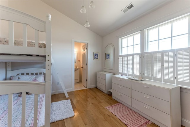 bedroom featuring lofted ceiling, light wood-style floors, visible vents, and ensuite bathroom