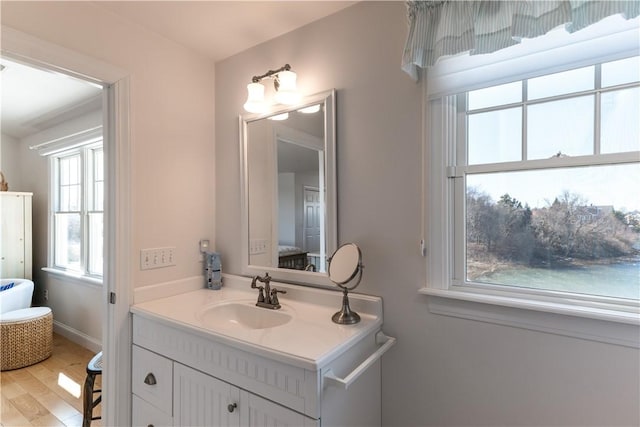 ensuite bathroom with baseboards, wood finished floors, vanity, and connected bathroom