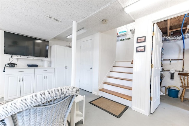 stairway featuring a paneled ceiling, finished concrete floors, and visible vents