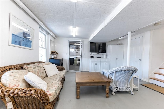 living area featuring stairs, baseboards, a paneled ceiling, and finished concrete floors