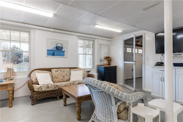 living room featuring visible vents, a drop ceiling, and concrete flooring