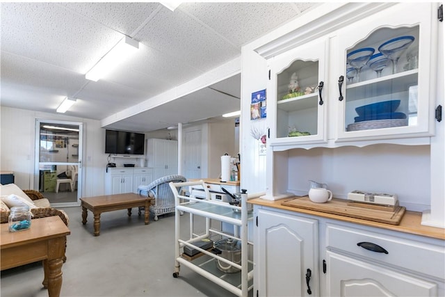 kitchen with finished concrete flooring, light countertops, glass insert cabinets, and white cabinetry