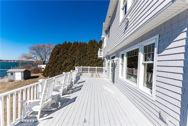 wooden deck with an outbuilding, a water view, and a shed