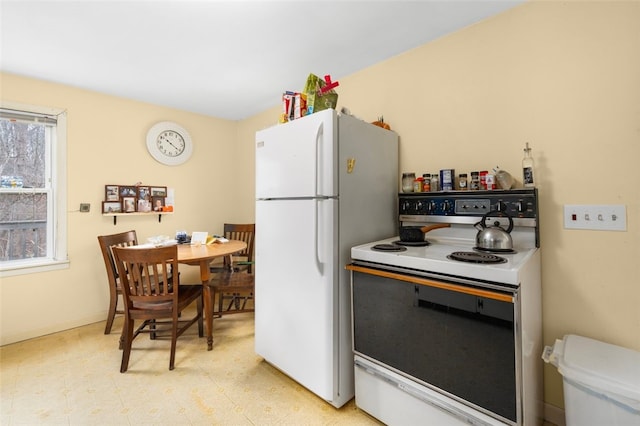 kitchen featuring light floors, freestanding refrigerator, baseboards, and electric range oven