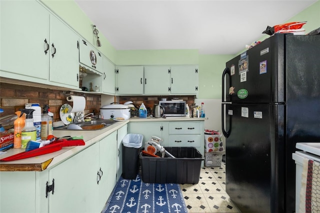 kitchen featuring light countertops, stainless steel microwave, freestanding refrigerator, a sink, and range