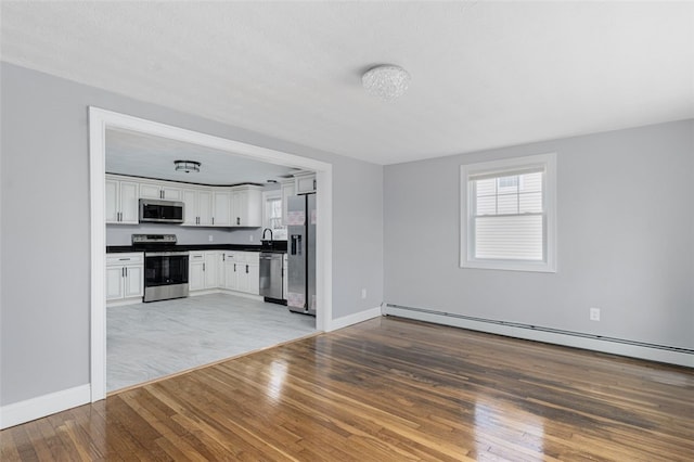 kitchen with dark countertops, a wealth of natural light, baseboard heating, appliances with stainless steel finishes, and hardwood / wood-style floors