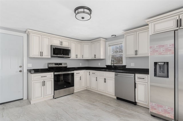 kitchen with dark countertops, appliances with stainless steel finishes, cream cabinetry, and a sink