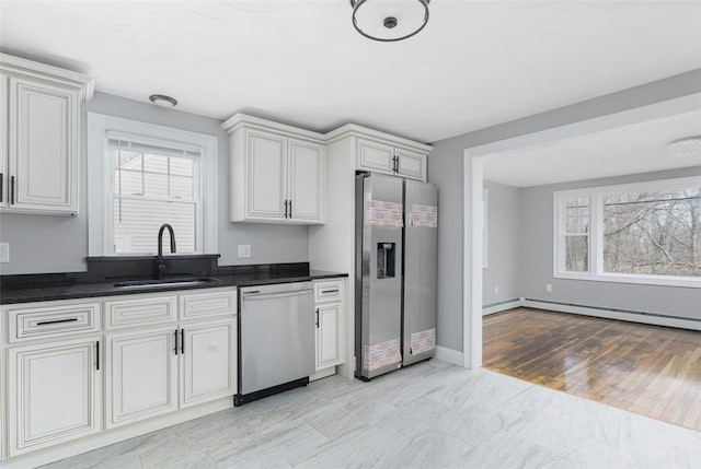 kitchen with a sink, baseboards, appliances with stainless steel finishes, light wood finished floors, and dark countertops